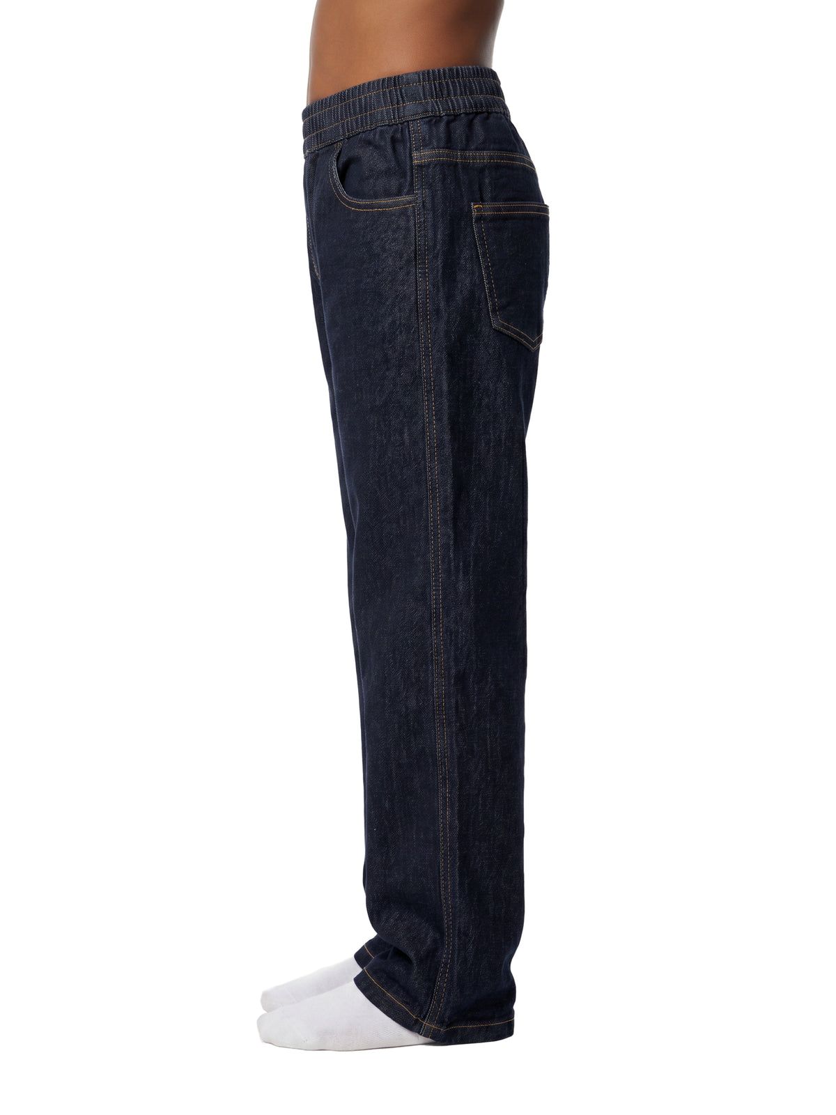 Side view of a person wearing dark indigo denim jogger pants with an elastic waistband and white socks, shown against a plain white background.