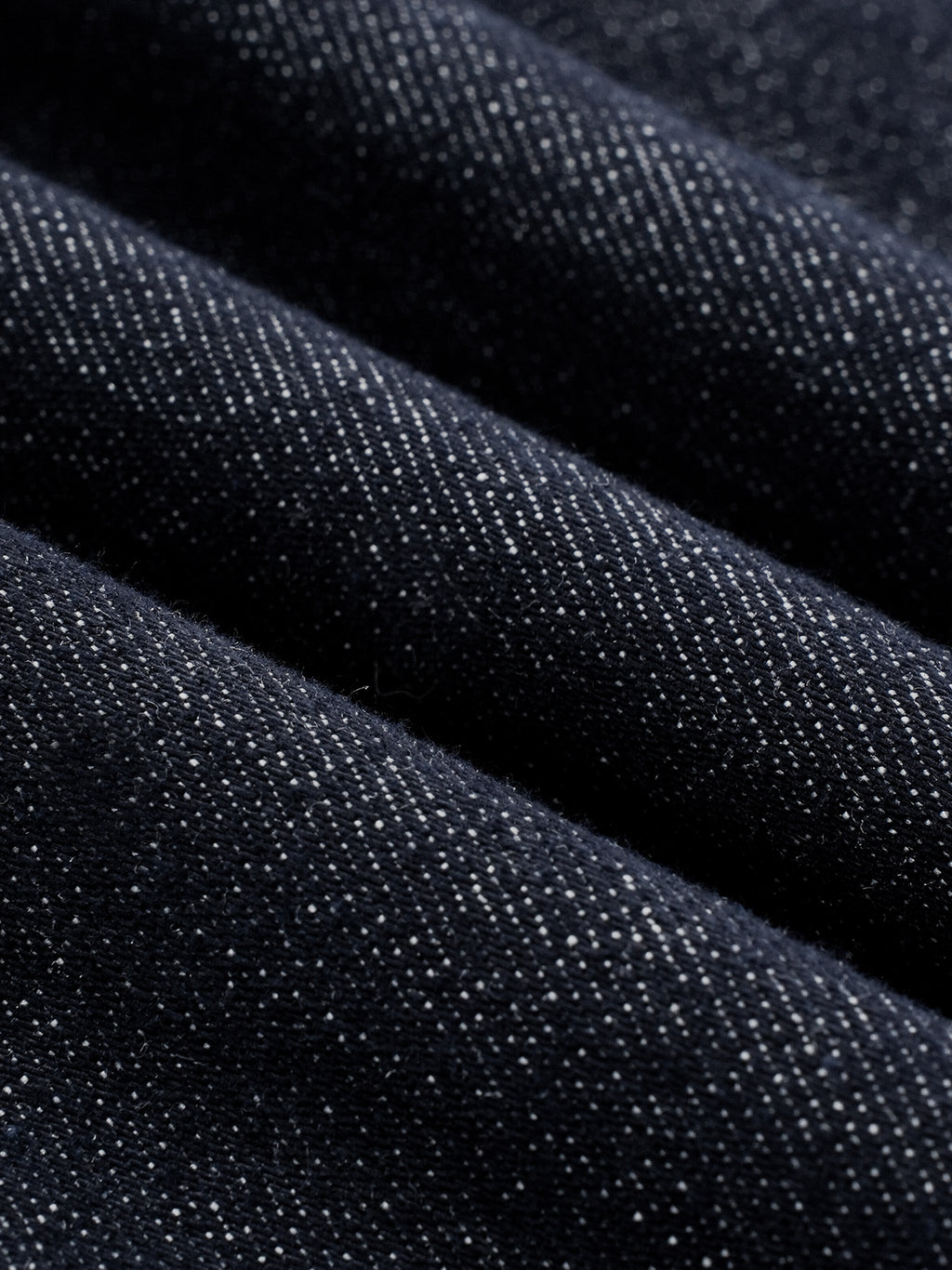 Close-up of dark indigo denim fabric with a visible twill weave texture, arranged in soft diagonal folds.