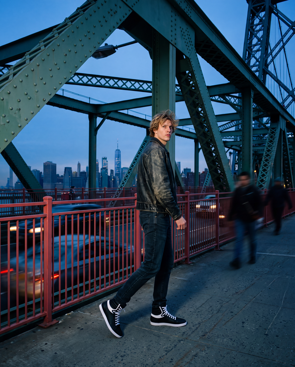 A man wearing a black leather jacket, straight-leg denim jeans, and P34K new wave bnw fashion high-top sneakers walks along a bridge path at dusk with the New York City skyline in the background.