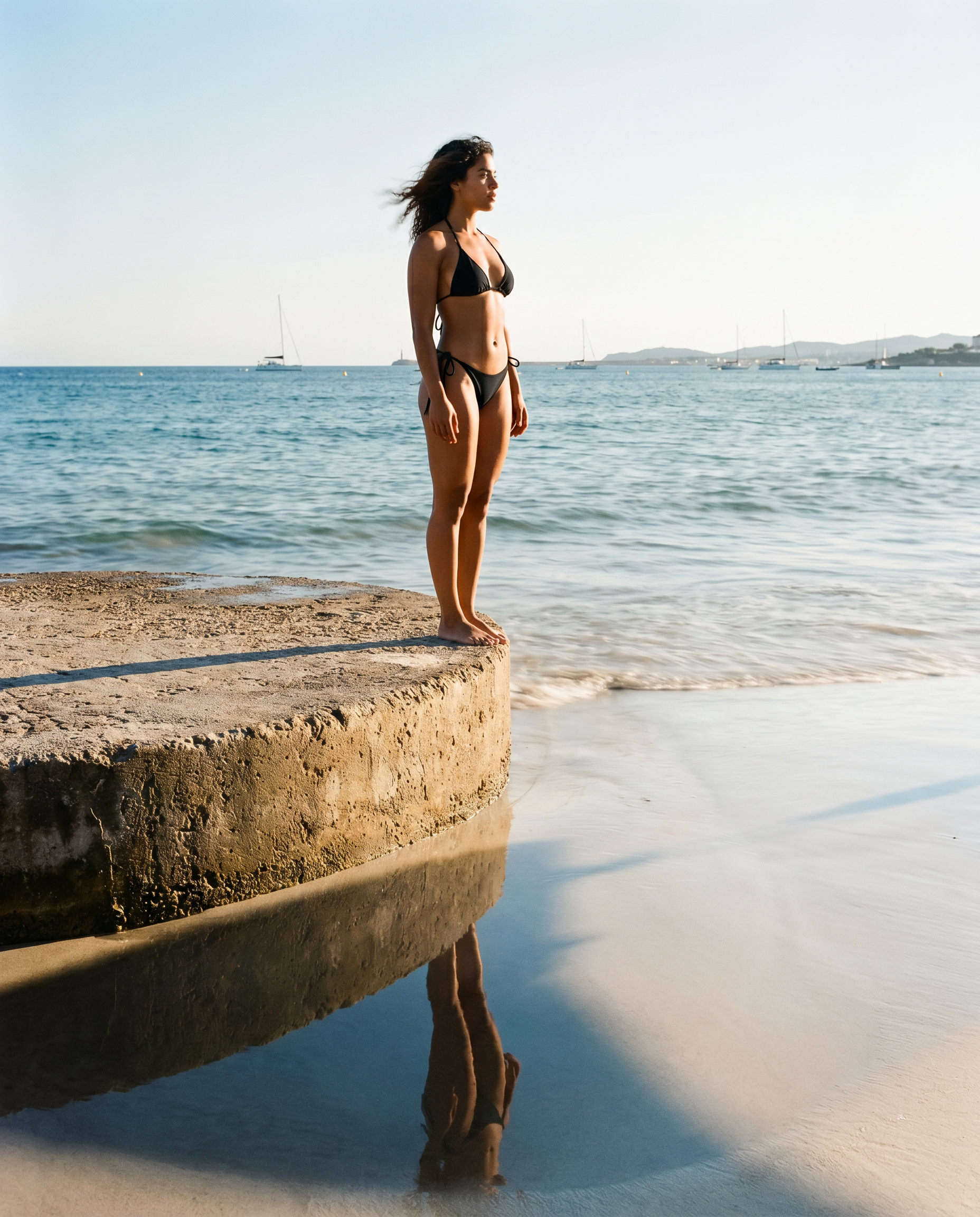 Woman in a black bikini standing on a rock by the ocean