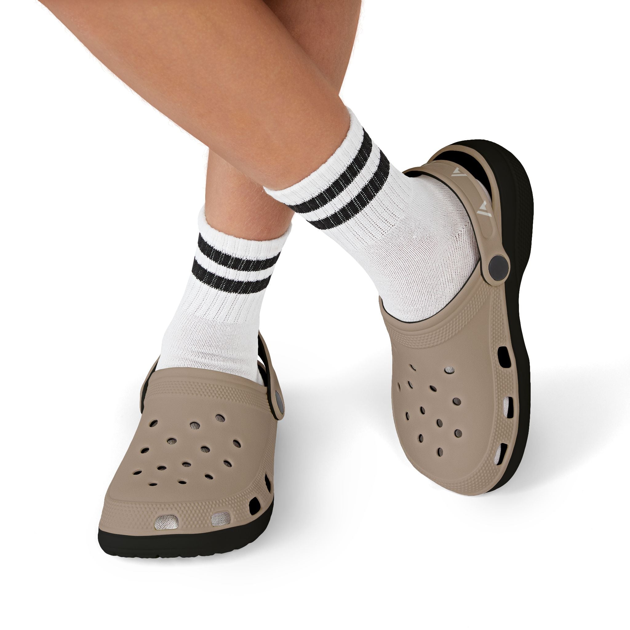 A person wearing taupe Croc-style clogs with black soles, paired with white crew socks featuring black stripes, shown against a plain white background.