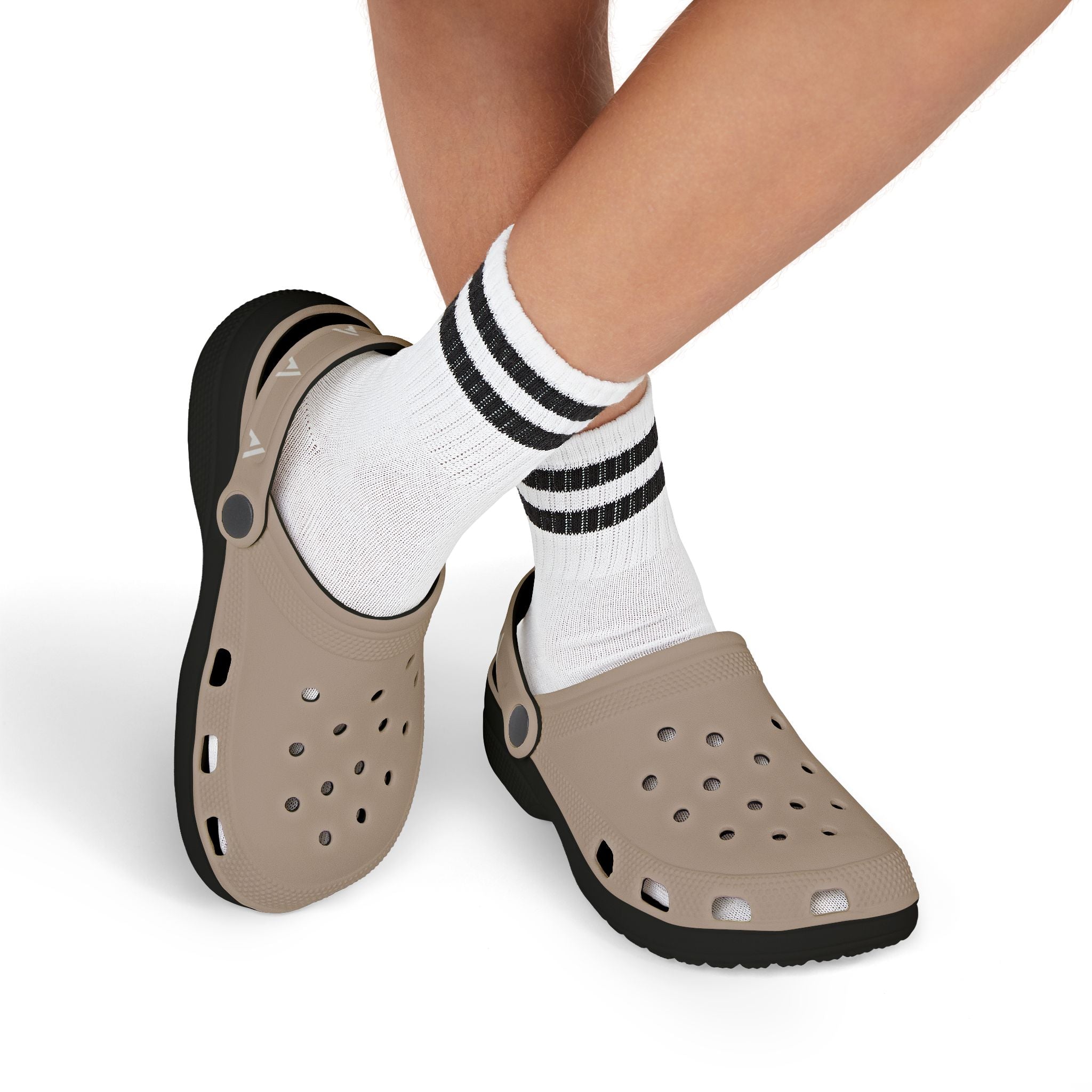 A pair of taupe foam clogs with black soles, shown on a model's feet wearing white crew socks with black stripes, against a white background.