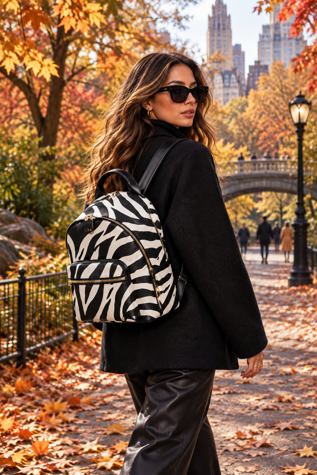 Four-panel product feature collage of a zebra-print backpack with black panels and gold-tone hardware. The panels show the front view with top carry handle, the side zipper opening, the interior zip pocket with sunglasses in the pocket, and the black bottom with round metallic feet.